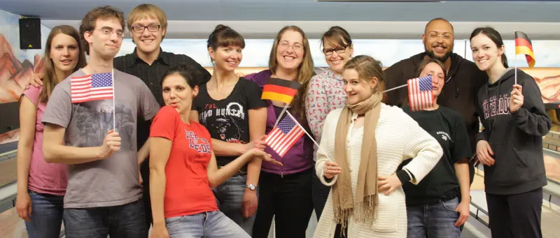 Group photo of participants of Bamberg Buddies having a good time at the bowling alley, waving German and US flags.