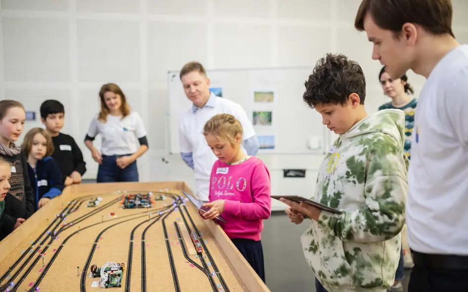 Kinder aus dem Workshop stehen mit den Betreuenden neben der Modelleisenbahn