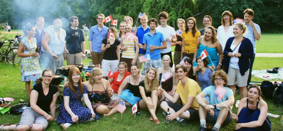 Group photo of participants of Bamberg Buddies having a good time at a barbecue party in the Hain Park, waving US and Canadian flags.