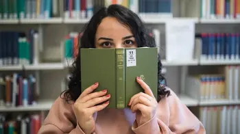 Studentin schaut ber den Rand eines Buches in der Bibliothek